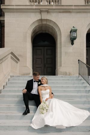 Wedding couple poses for romantic photos on elegant light stone steps leading to building entrance.