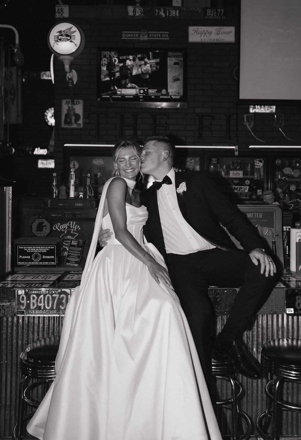 Playful black and white dance sequence showing bride in white gown and groom in dark suit at a dimly lit bar venue.