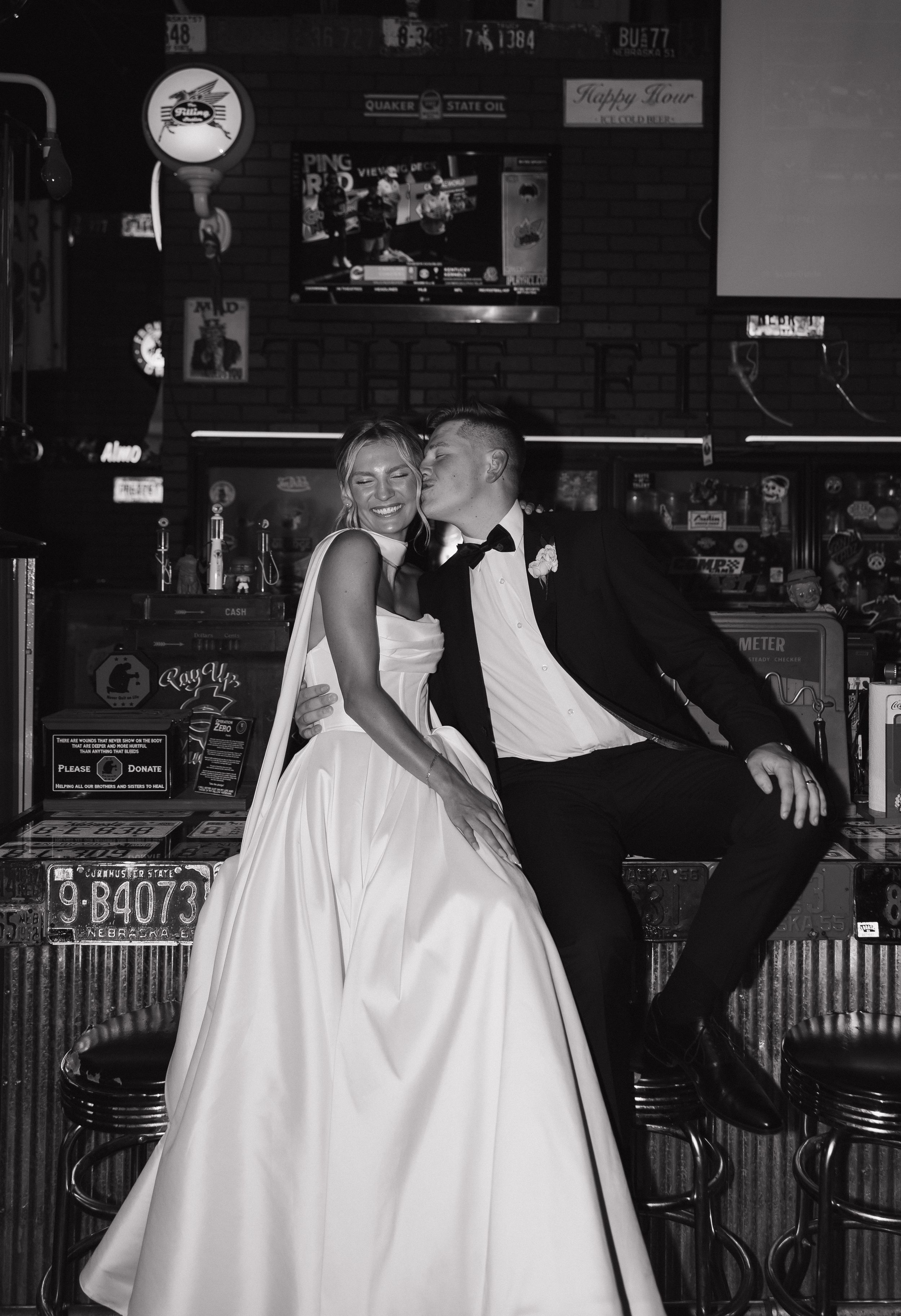 Playful black and white dance sequence showing bride in white gown and groom in dark suit at a dimly lit bar venue.