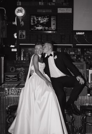 Playful black and white dance sequence showing bride in white gown and groom in dark suit at a dimly lit bar venue.