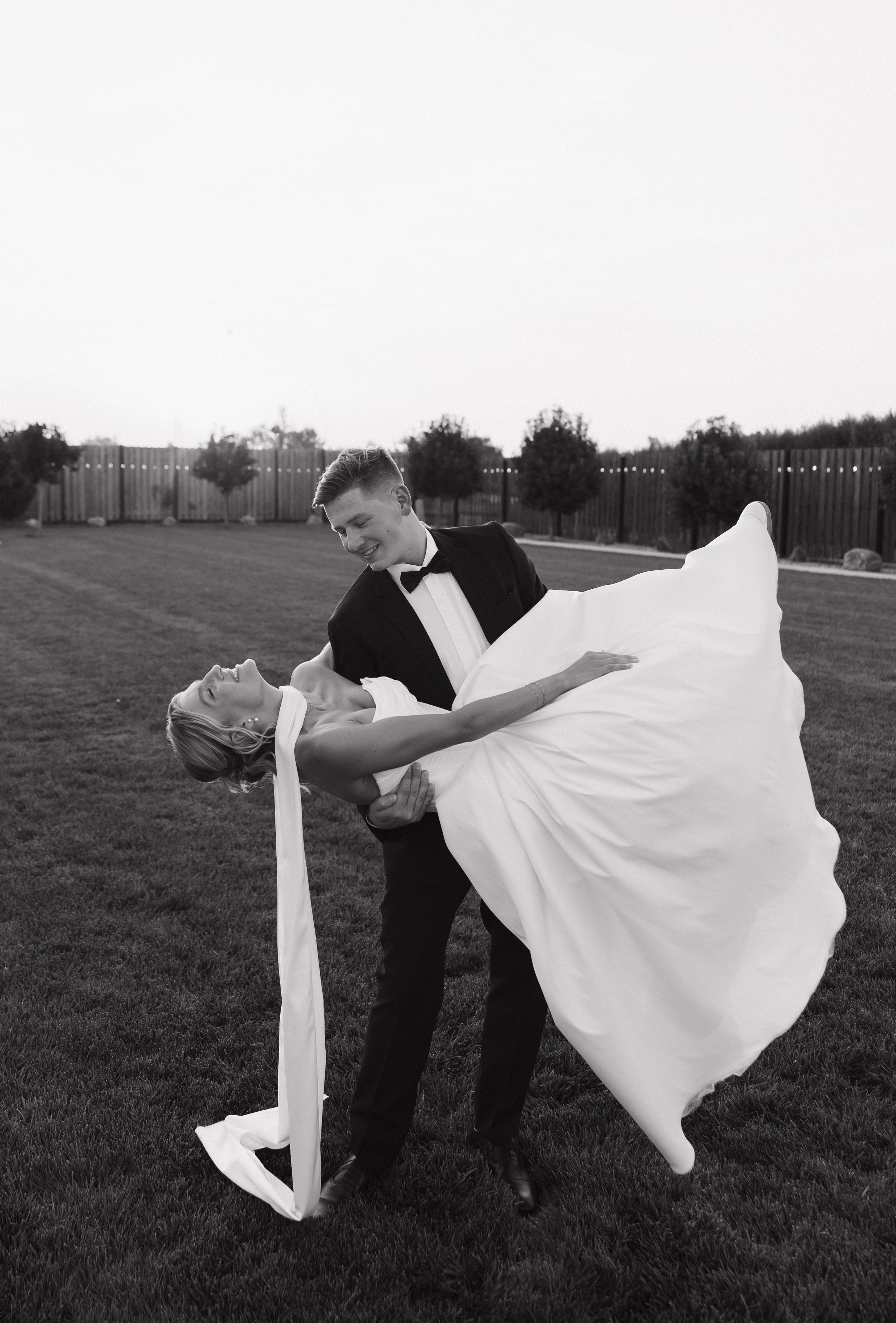 Dramatic black and white photo of a groom dipping his bride in an elegant dance pose on a lawn.