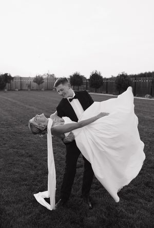 Dramatic black and white photo of a groom dipping his bride in an elegant dance pose on a lawn.