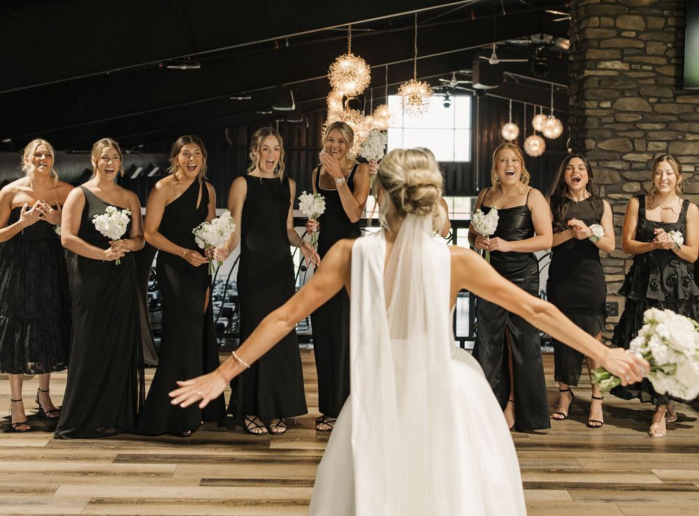 A group of bridesmaids in black dresses pose together with a bride in white during a wedding celebration.