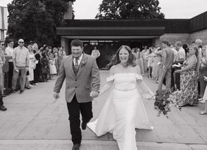 A couple walks down a path surrounded by guests as the bride's white dress flows in the breeze.