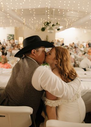 Newlyweds share a tender kiss under twinkling fairy lights at their wedding reception.