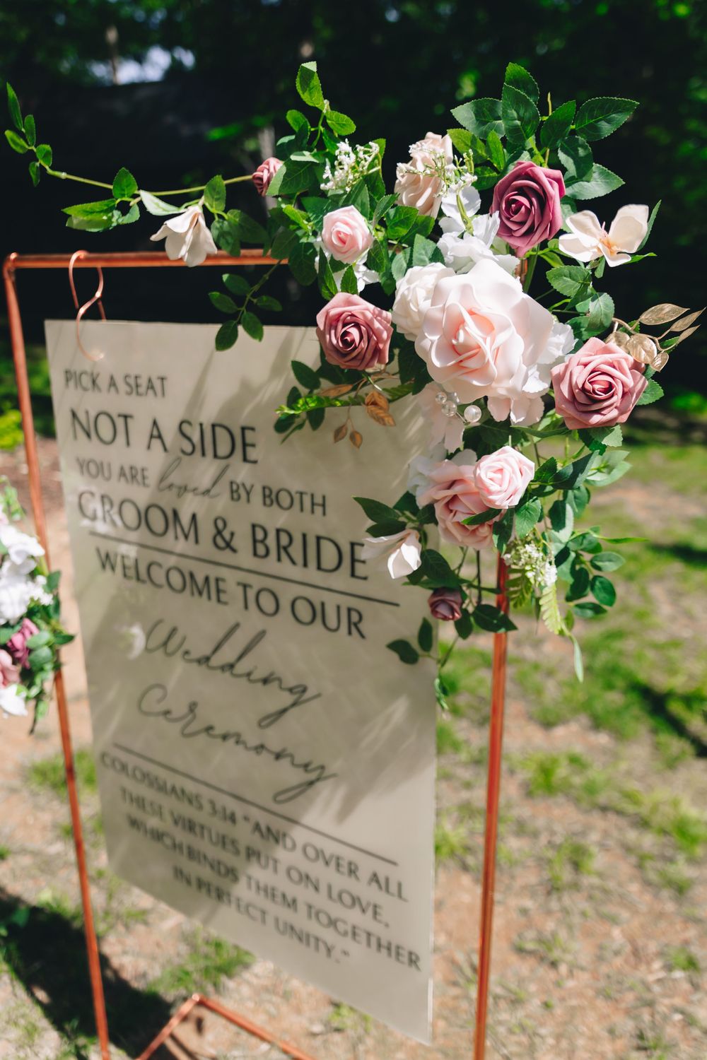Wedding welcome signs decorated with pink roses and greenery on copper stands.