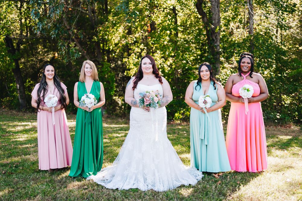 Bridal party in pastel pink and mint green dresses posed together in a sunny outdoor setting.
