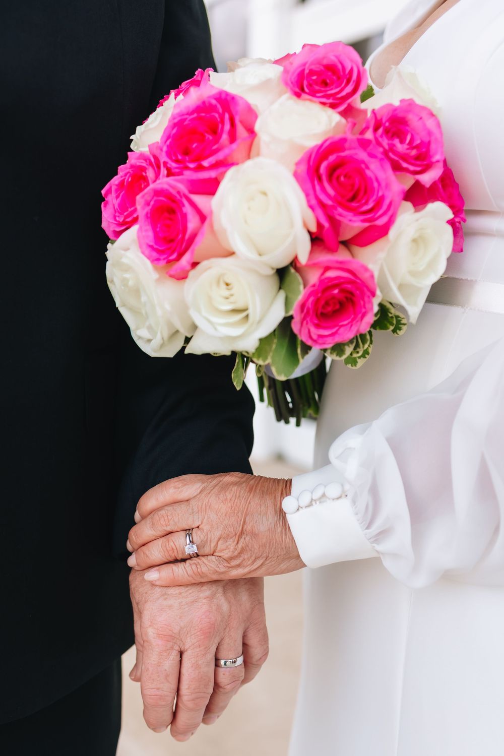 Wedding bouquet of pink and white roses held with hands showing wedding rings.