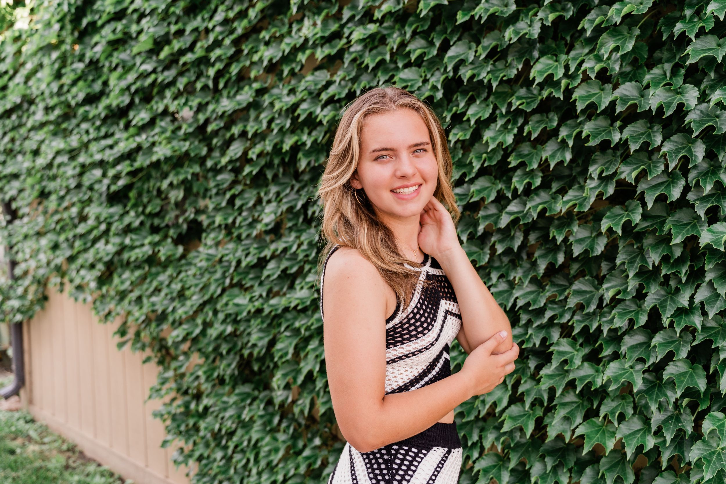 A senior photo session with ivy-covered walls and black and white dress creates an elegant outdoor portrait setting.