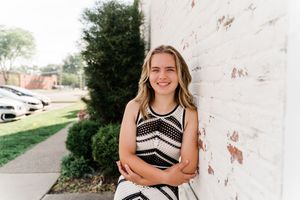 Senior portrait photography session against a rustic white wall backdrop in an outdoor setting.