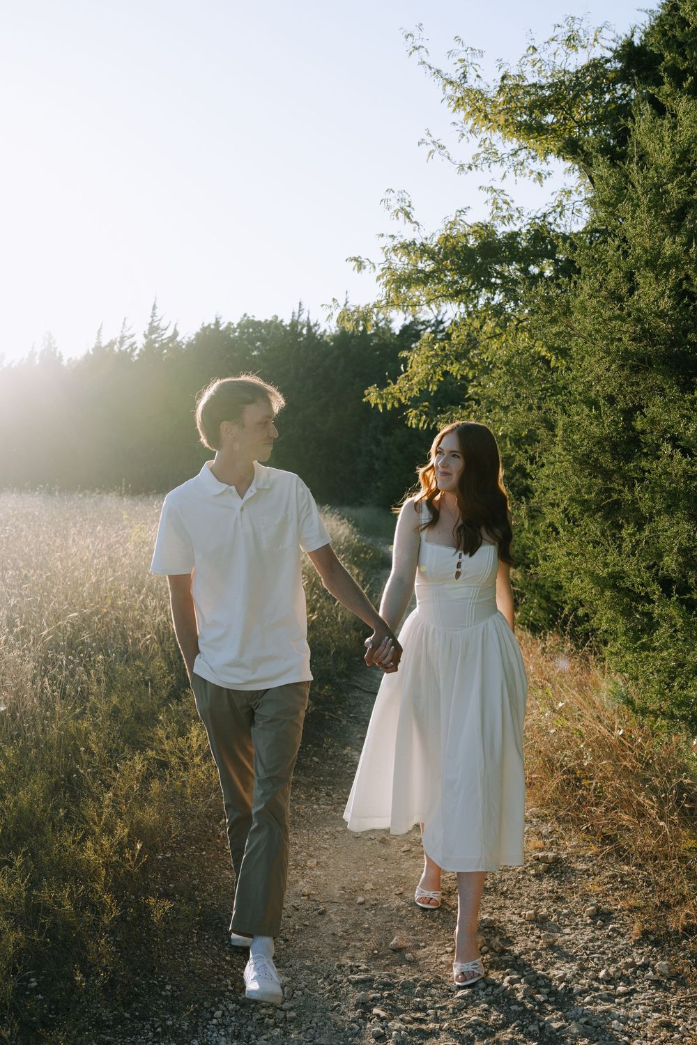 A couple walking together on a sunlit dirt path through a golden field at sunset, captured in a romantic sequence.