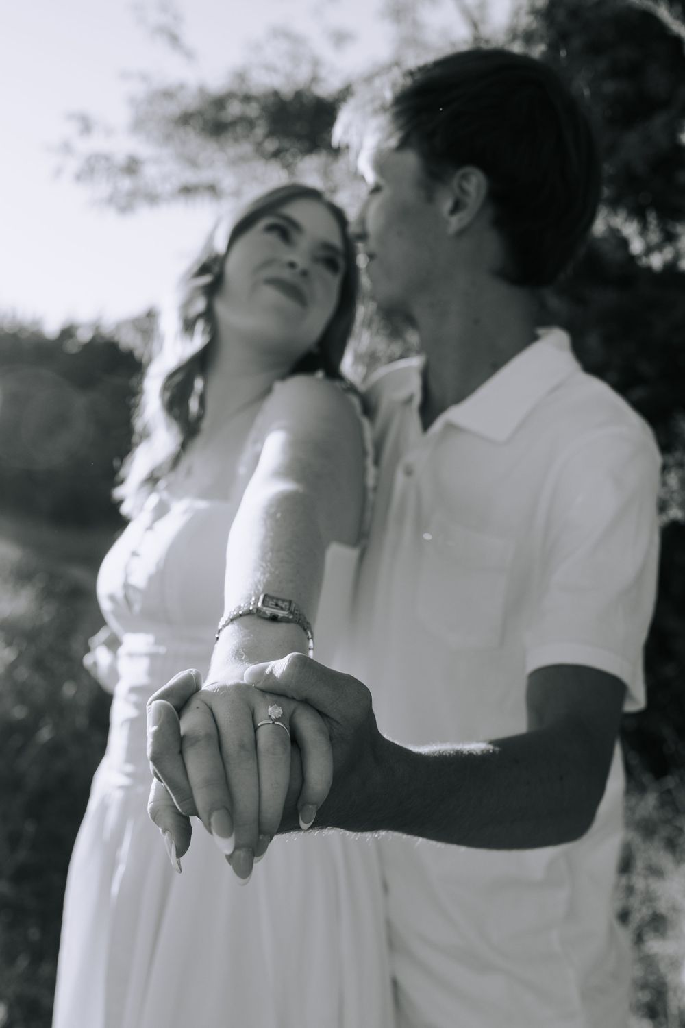 Black and white romantic photoshoot showing couple embracing while displaying engagement ring.