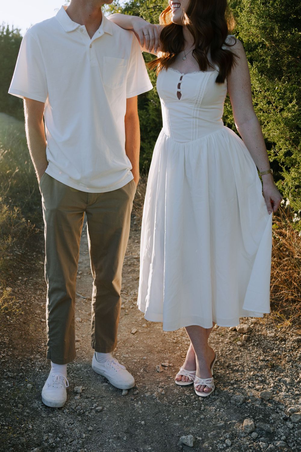 Couple in white outfits photographed from waist down standing together on a gravel path.
