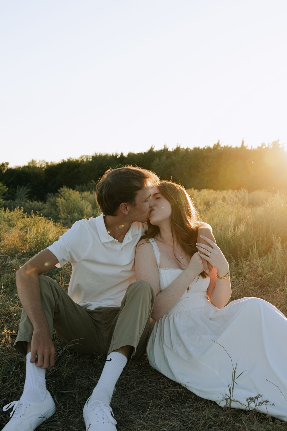 Intimate moment between couple sitting in field at sunset wearing white and khaki.