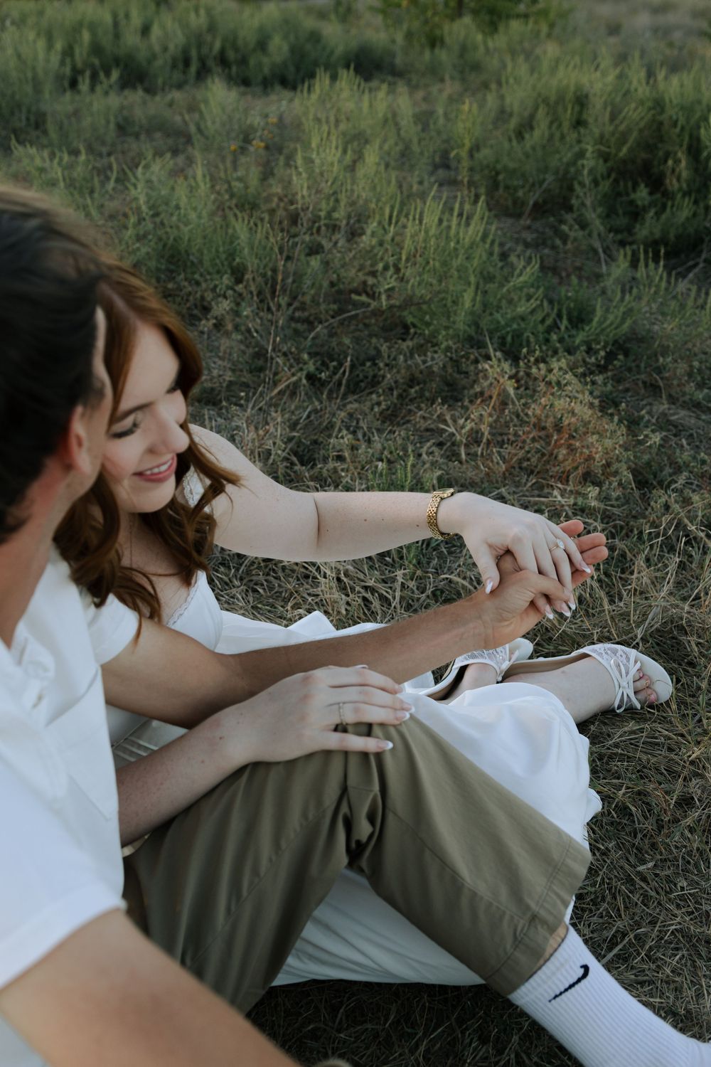 A couple laughs and plays together while laying in a grassy field during a romantic outdoor photoshoot.