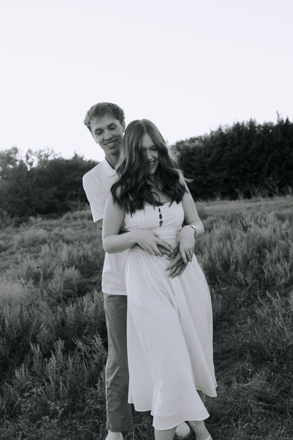 A romantic black and white photo series showing a couple embracing in a grassy field at sunset.