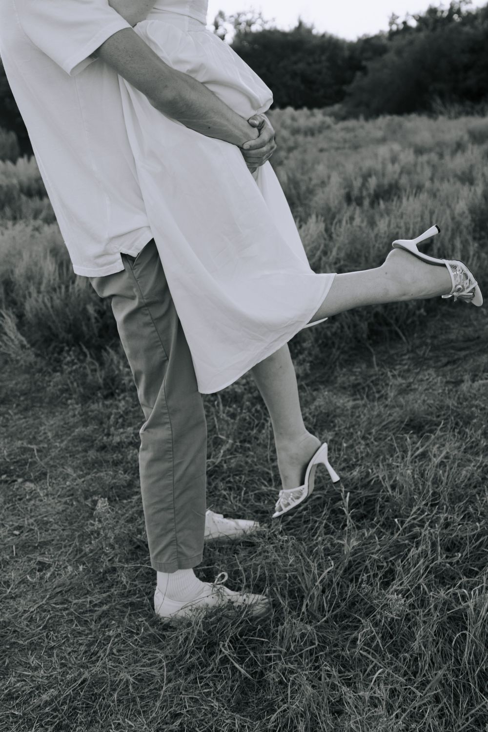 Black and white photo showing playful footwork between a couple wearing white and khaki outfits outdoors.