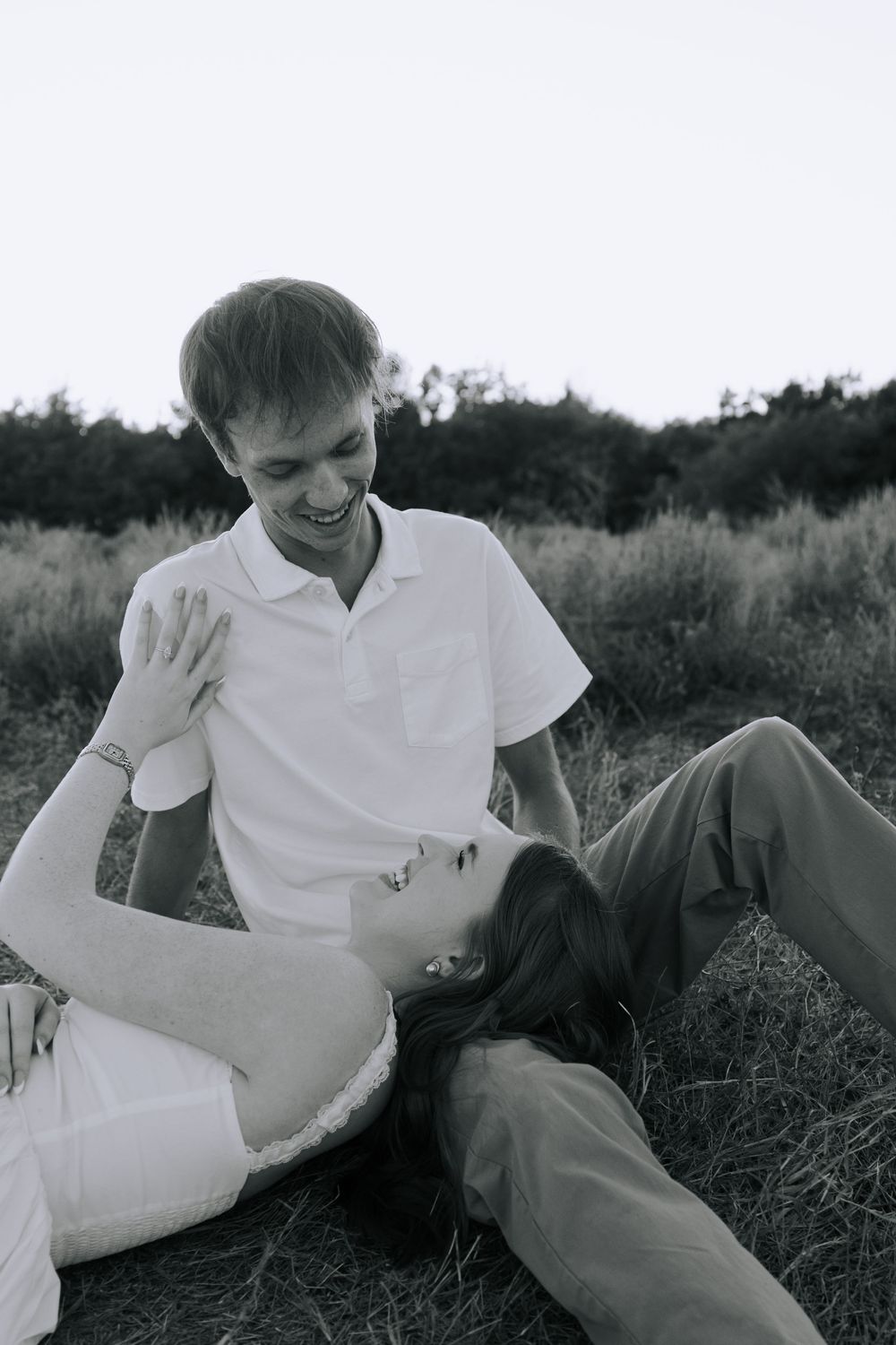 Black and white portrait of a couple sharing intimate laughs while relaxing in tall grass.