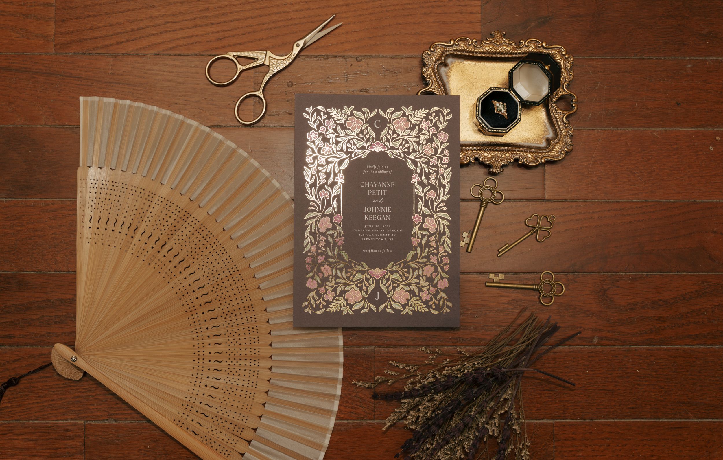 Elegant vintage wedding invitation with floral laser-cut design, displayed with a wooden fan, scissors, and dried botanicals.