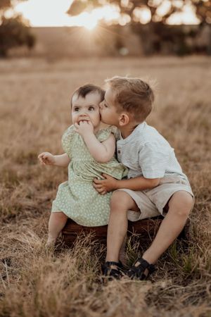 Two young children sharing a sweet moment while sitting in dry grass at sunset.