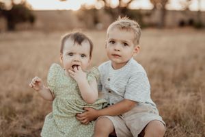 Siblings playing together in a sunlit field during golden hour.