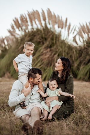 Family of four relaxing together in a grass field during sunset.