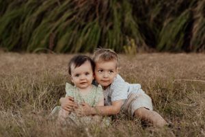 Two small children sitting side by side in dry grass during golden hour photography session.