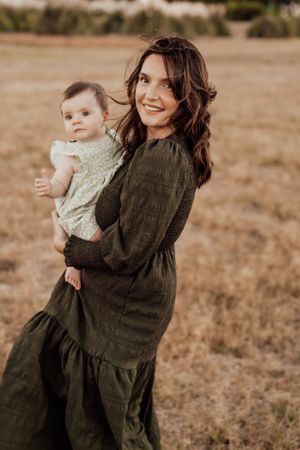 Mother in dark dress embraces child in soft lighting during outdoor photo session.
