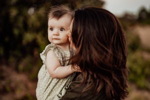 Tender family moment captured in warm tones against natural outdoor backdrop.