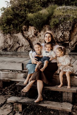 Family relaxing together on rustic wooden bench near rocky beach cliffs.
