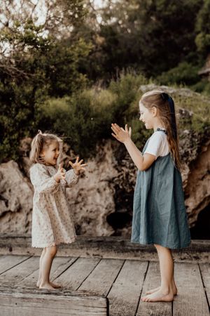 Two young children playing and clapping together on a wooden deck in nature.