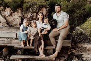 Family sitting together on wooden deck with their black dog near rocky cliffs.