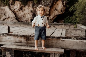 Small child standing barefoot on wooden dock with rocky cliff backdrop.
