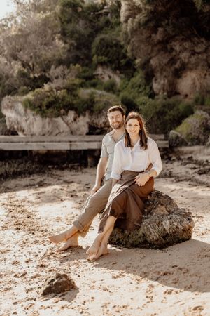 Couple sitting together on beach rocks during golden hour photoshoot.