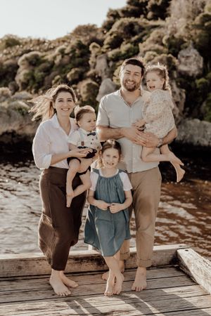 Family portrait on wooden dock with rocky coastal backdrop.