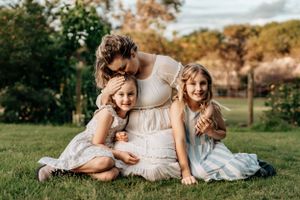 Family dressed in white and cream colored outfits laying together on grass outdoors.