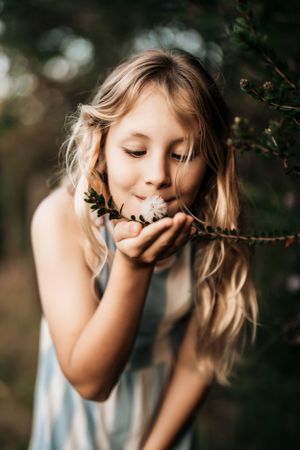 Young girl in a blue dress poses playfully against a natural outdoor backdrop.