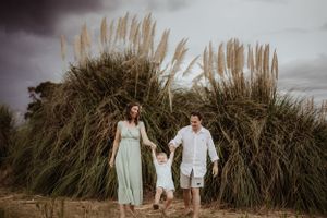 A family holds hands while walking together through tall pampas grass at sunset.