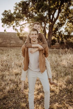 Couple sharing a playful moment outdoors in a field with golden sunlight and trees in the background.