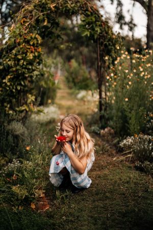 Child in a blue dress laying in the grass during golden hour surrounded by nature.