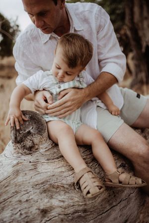 A gentle teaching moment shared between parent and child on a weathered log.
