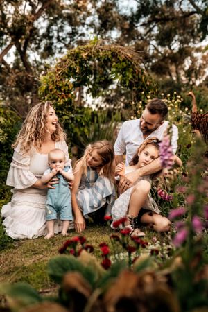 A loving family moment captured in a garden setting with pink flowers and natural sunlight.