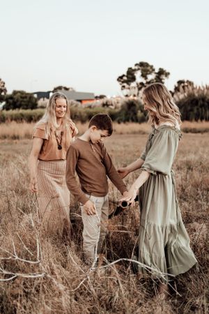 Family in neutral-toned outfits walking and playing together in a grassy field at sunset.
