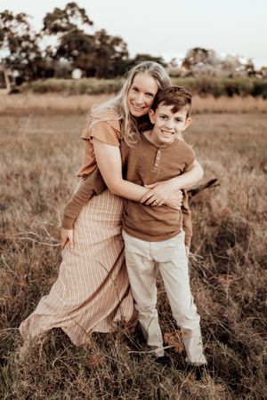 Family wearing earth tones shares playful moments together outdoors in a rustic field setting.