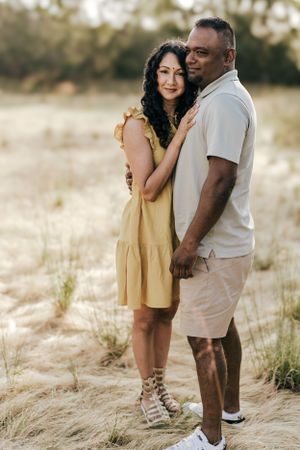 Couple embracing in golden field during sunset photoshoot.