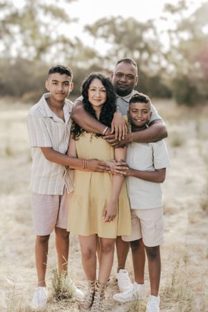 Family of four posing together in sunlit field during golden hour.