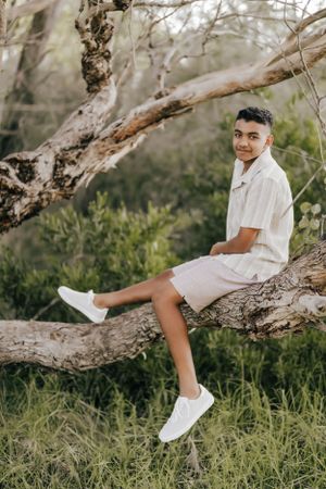 Someone in white sits casually on a fallen tree branch in a natural outdoor setting.