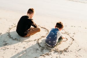 Two people sitting close together on pristine white sand at the beach.