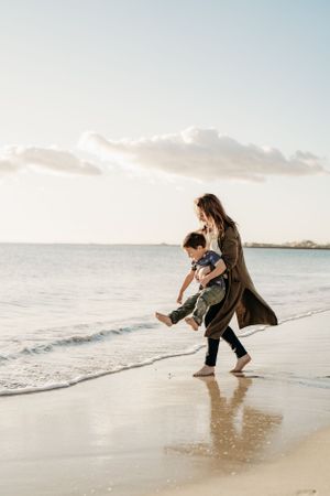 Person and child playing in the shallow waves at sunset on a beautiful beach.