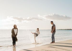 Family members running and playing together along the shoreline at sunset.